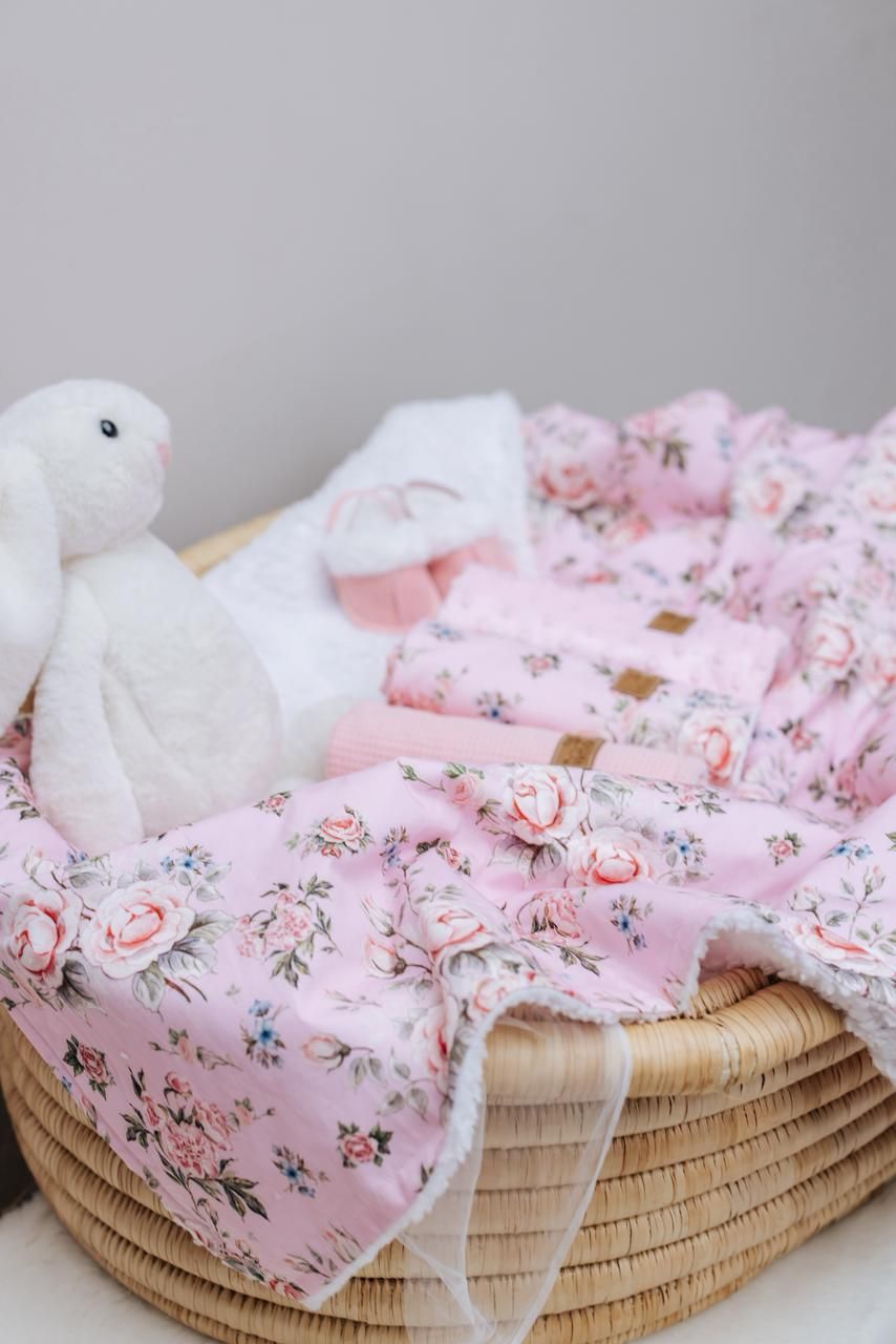 Pink floral baby blanket with white plush bunny displayed in woven basket.