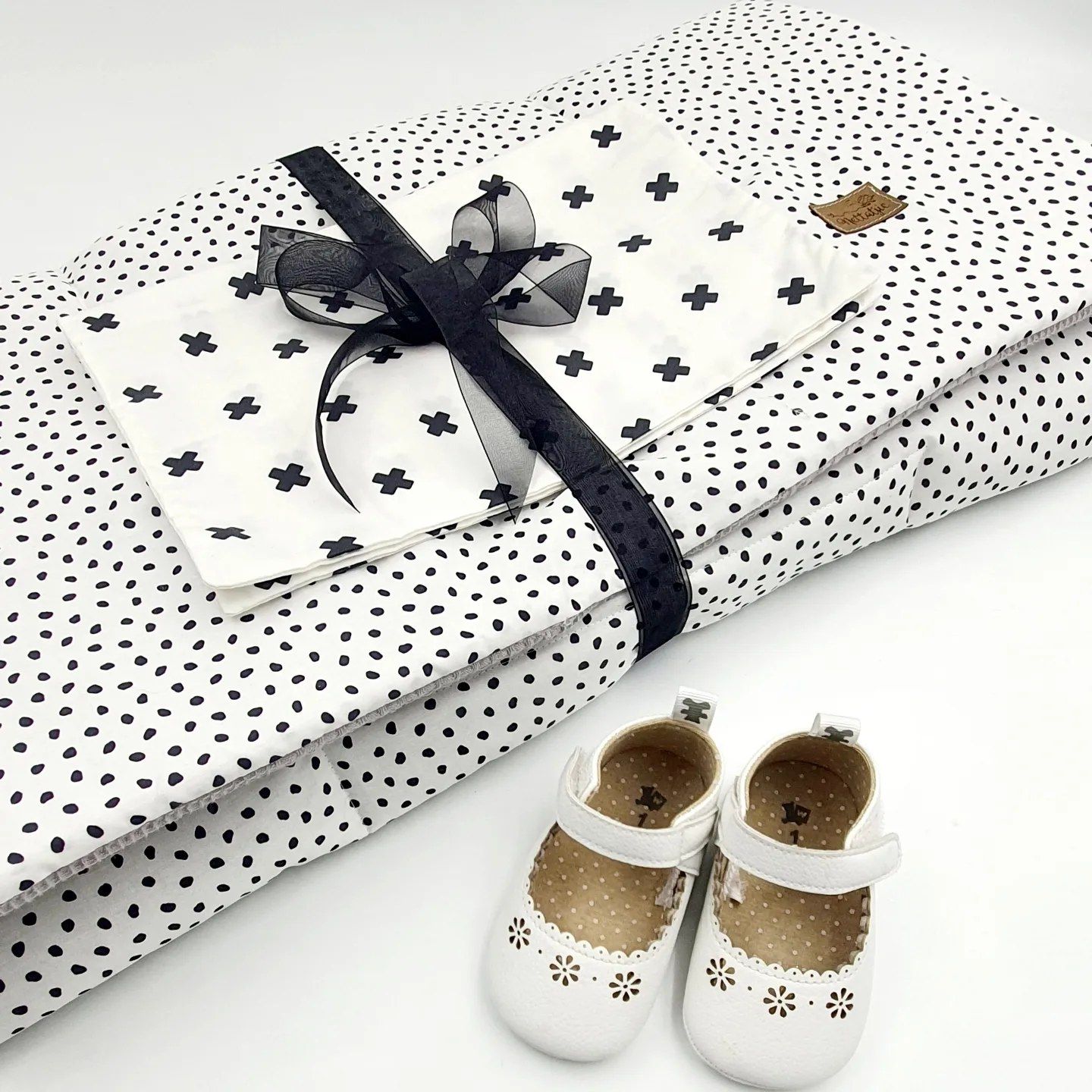 White and black polka dot gift wrap with stars pattern and black ribbon bow next to tiny white baby shoes.