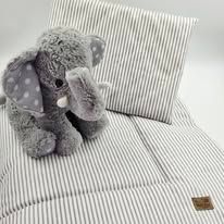A plush gray elephant toy sits on a striped fabric surface with a brown label visible in the corner.