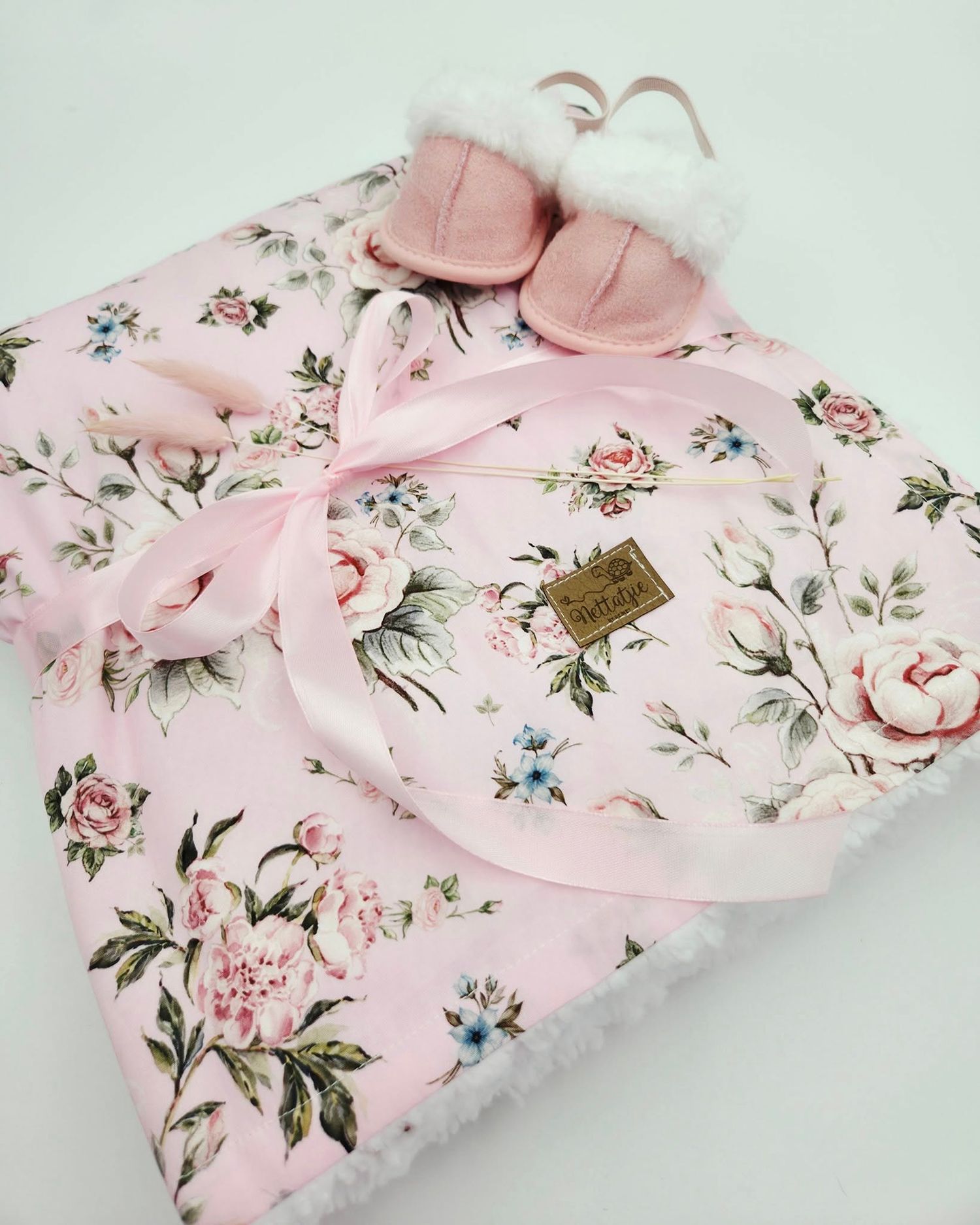 Pink floral baby blanket with delicate rose print and matching accessories on white background.