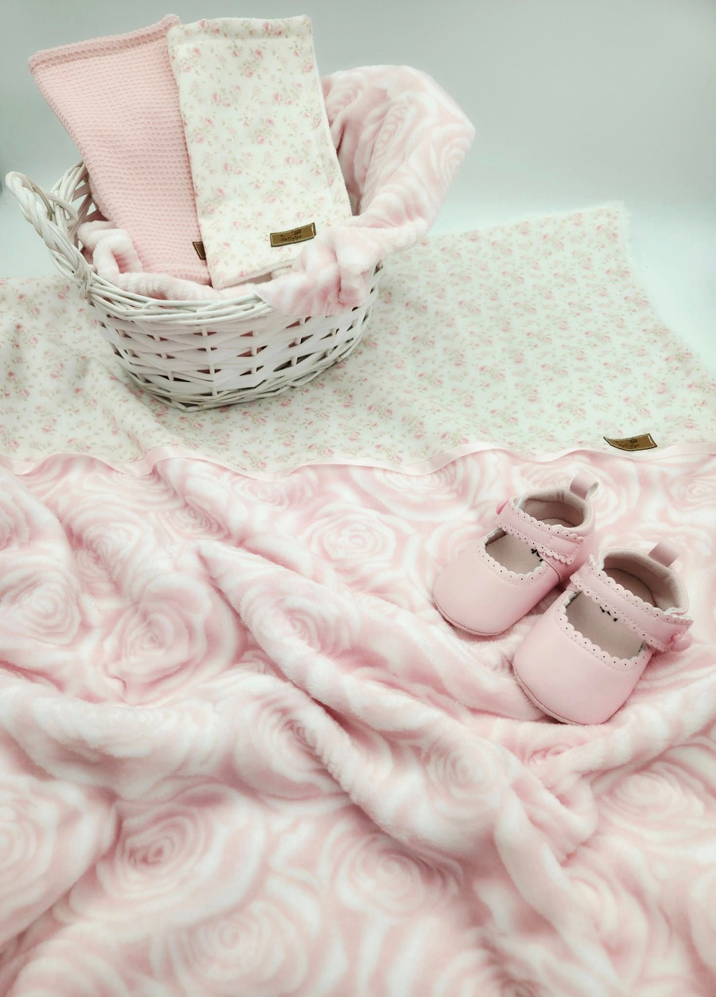 Pink rose pattern minky blanket with matching baby shoes displayed in white basket.