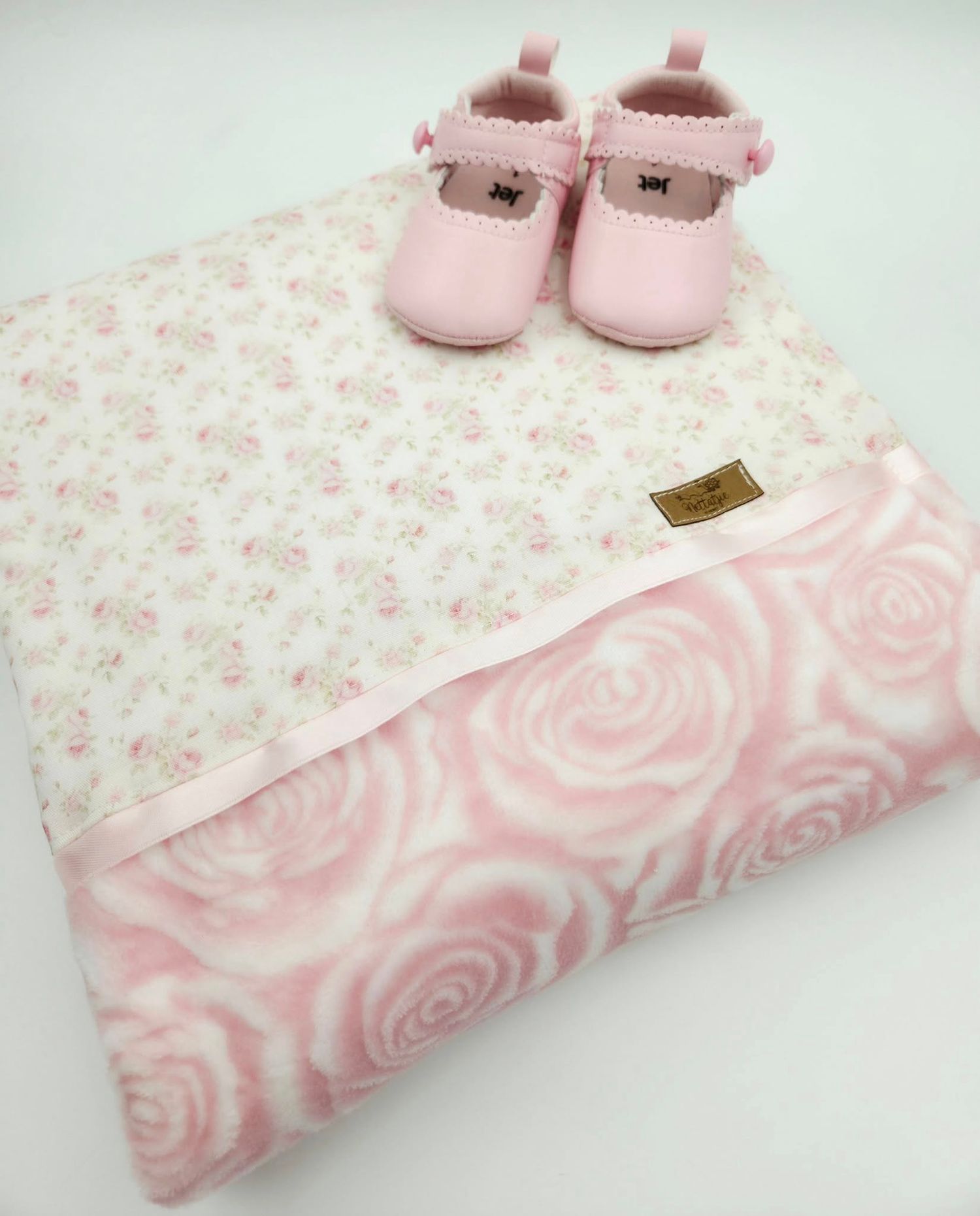 Soft pink rose embossed minky blanket with matching baby shoes on white surface.