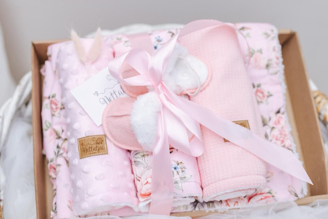 Pink floral baby blankets with white satin bows being prepared for packaging.