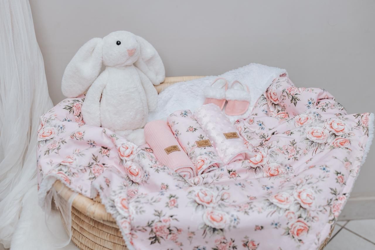 White plush bunny sitting on pink floral bedding in woven basket.