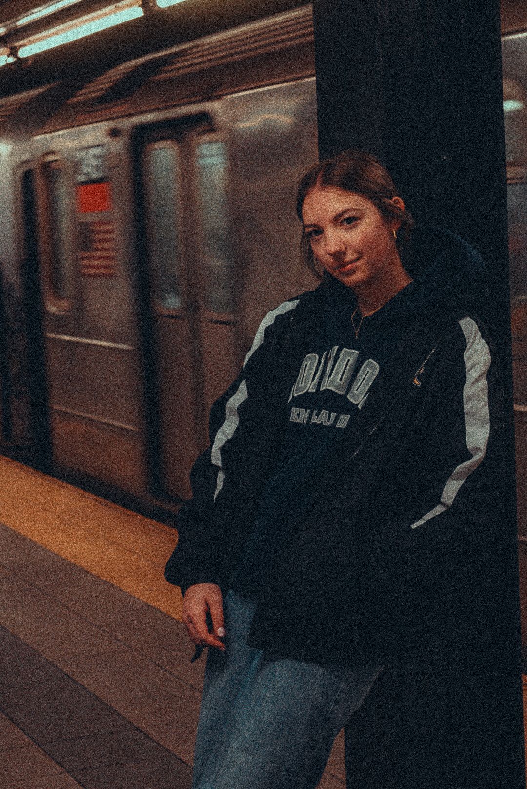 Moody subway station scene with person in black hoodie against dimly lit platform.