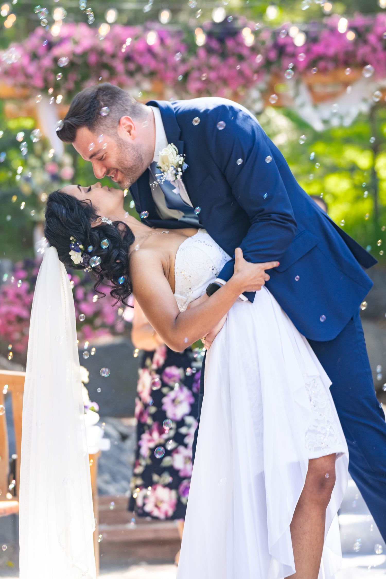Photo of groom dipping and kissing bride at a wedding with bubbles and pink flowers.