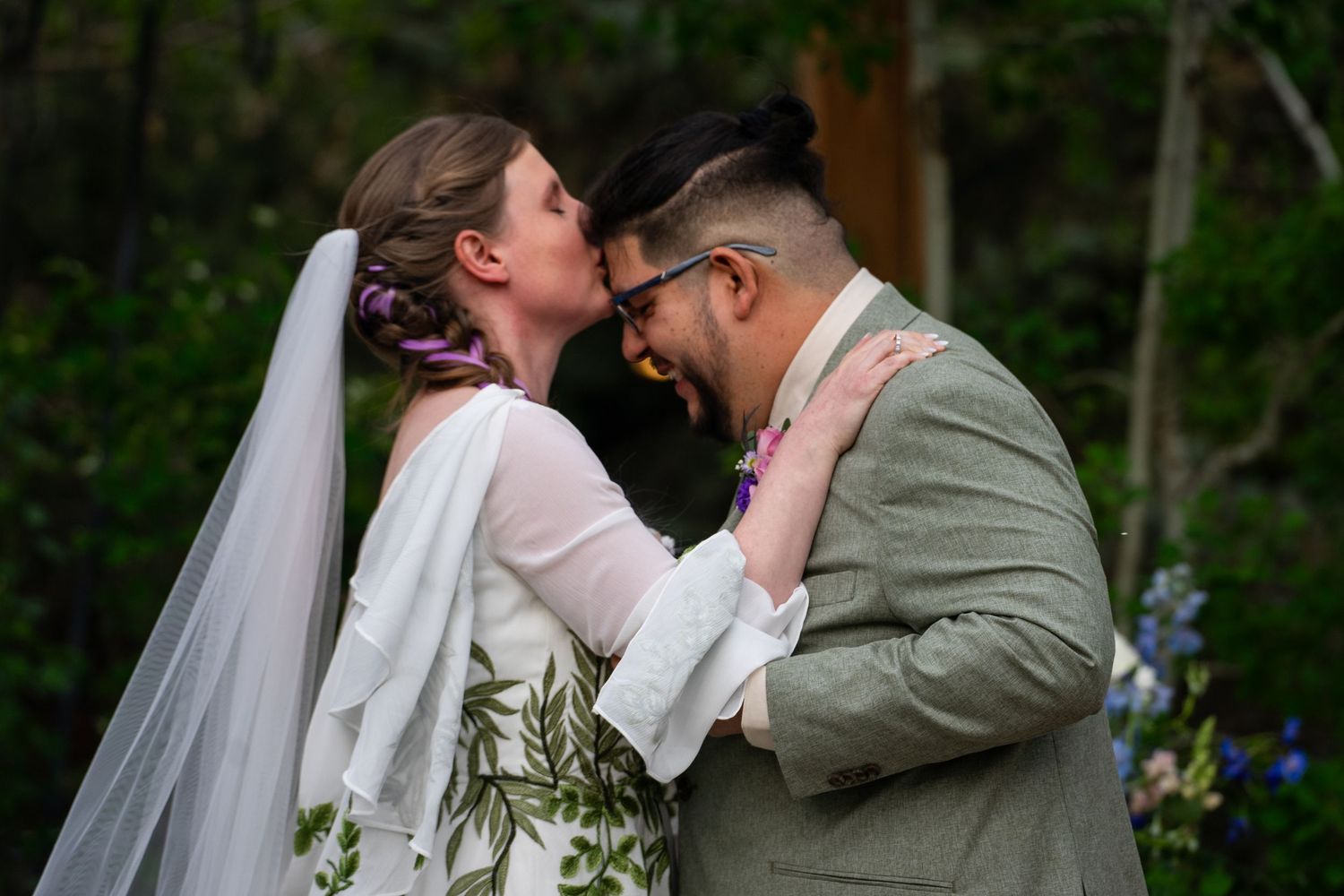A tender moment captured between a bride and groom during their outdoor wedding ceremony in a wooded setting.