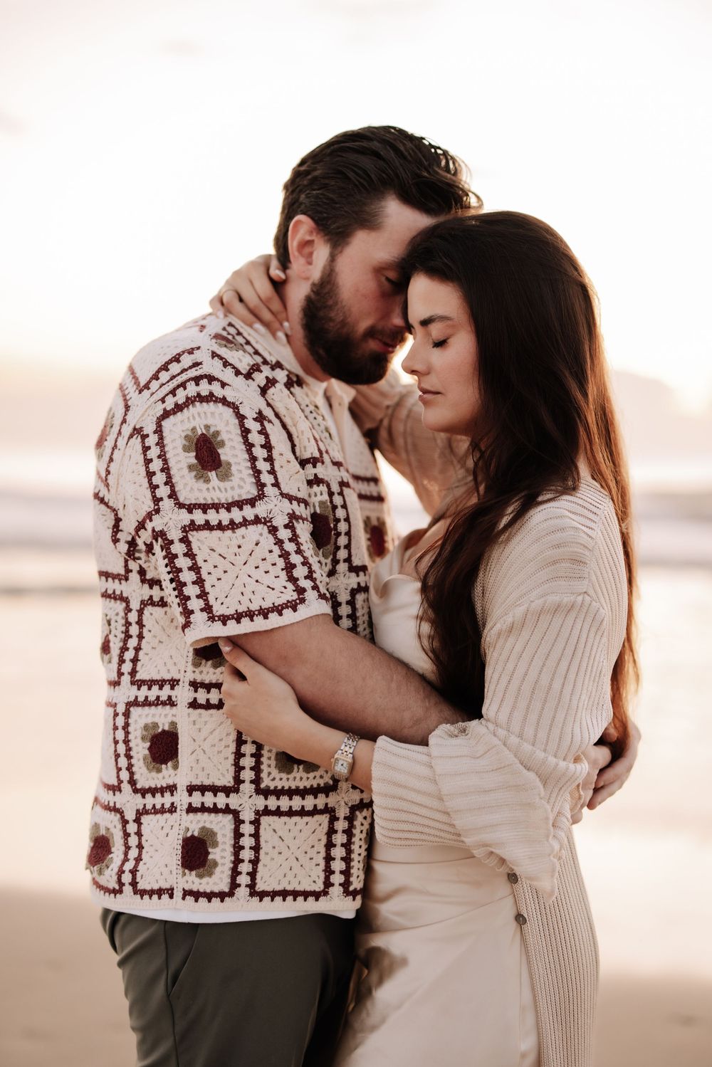 Romantic couple in sweaters embrace tenderly on a beach at sunset in a series of intimate poses.