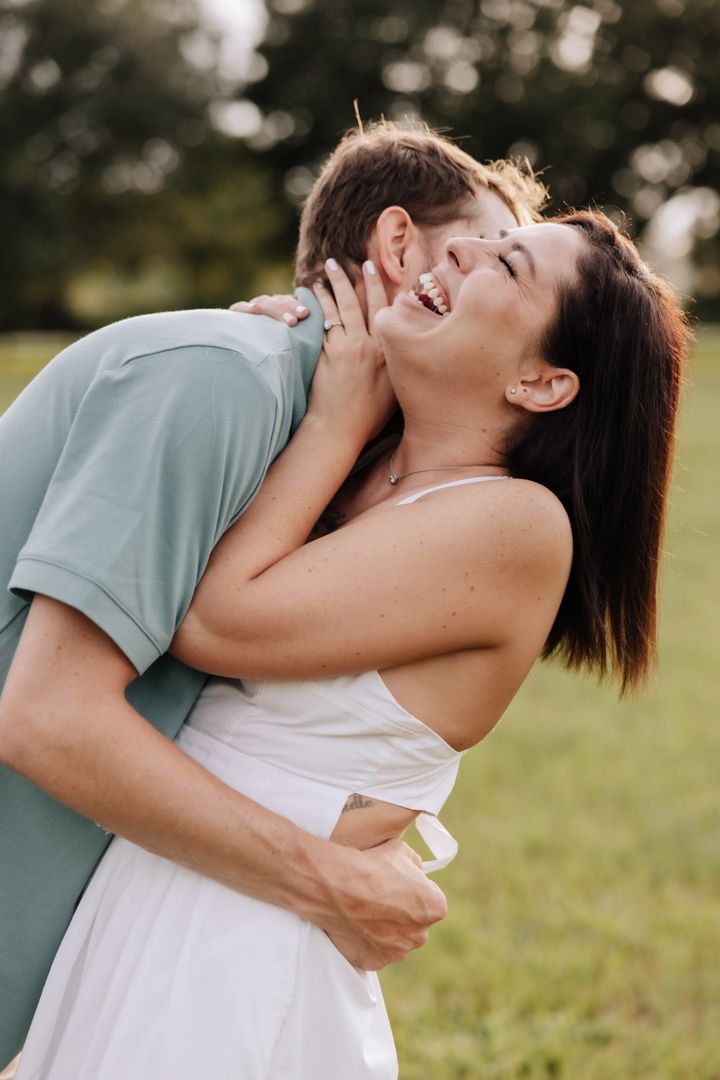 A couple in white and mint green outfits share tender embraces while laughing together in a sunny outdoor setting.