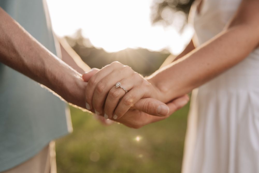 A close-up shot of two people holding hands outside with a wedding ring visible in warm sunlight.