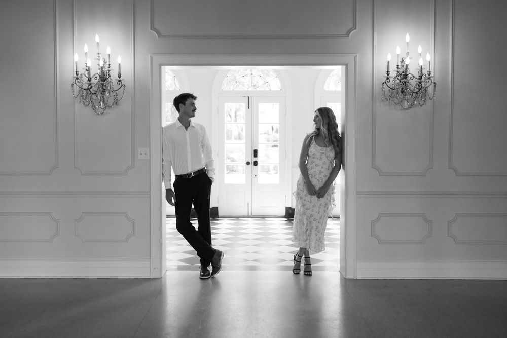 Black and white photo of a couple standing in an elegant doorway, facing each other in a romantic setting.