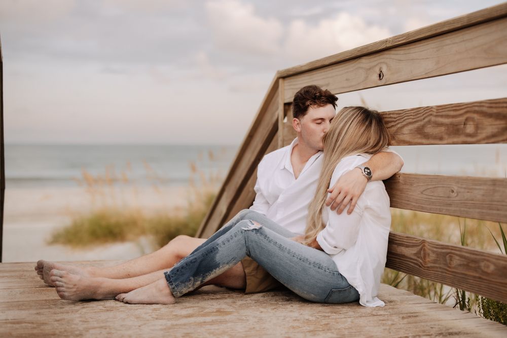 A couple relaxes together on a wooden bench at the beach during golden hour.