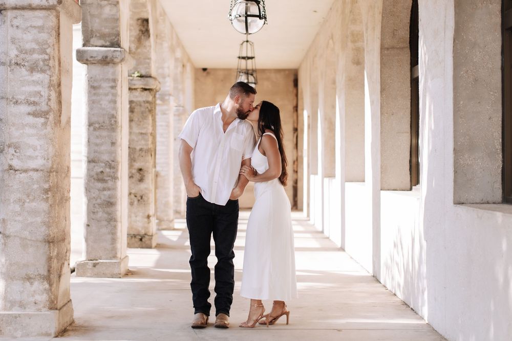 Couple embraces while standing in a beautiful white stone colonnade hallway with arched architecture.