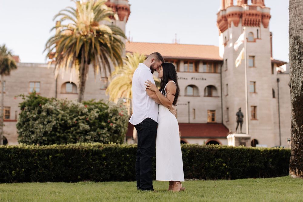 A couple shares an intimate moment in front of a Spanish colonial style building with palm trees and manicured gardens.