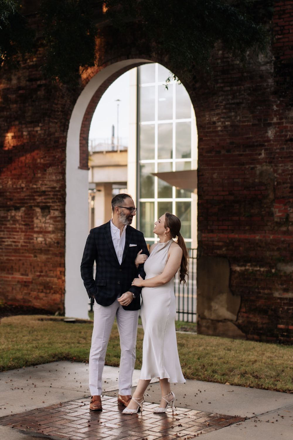 A couple in coordinated white and navy outfits shares romantic moments against a rustic brick wall backdrop.