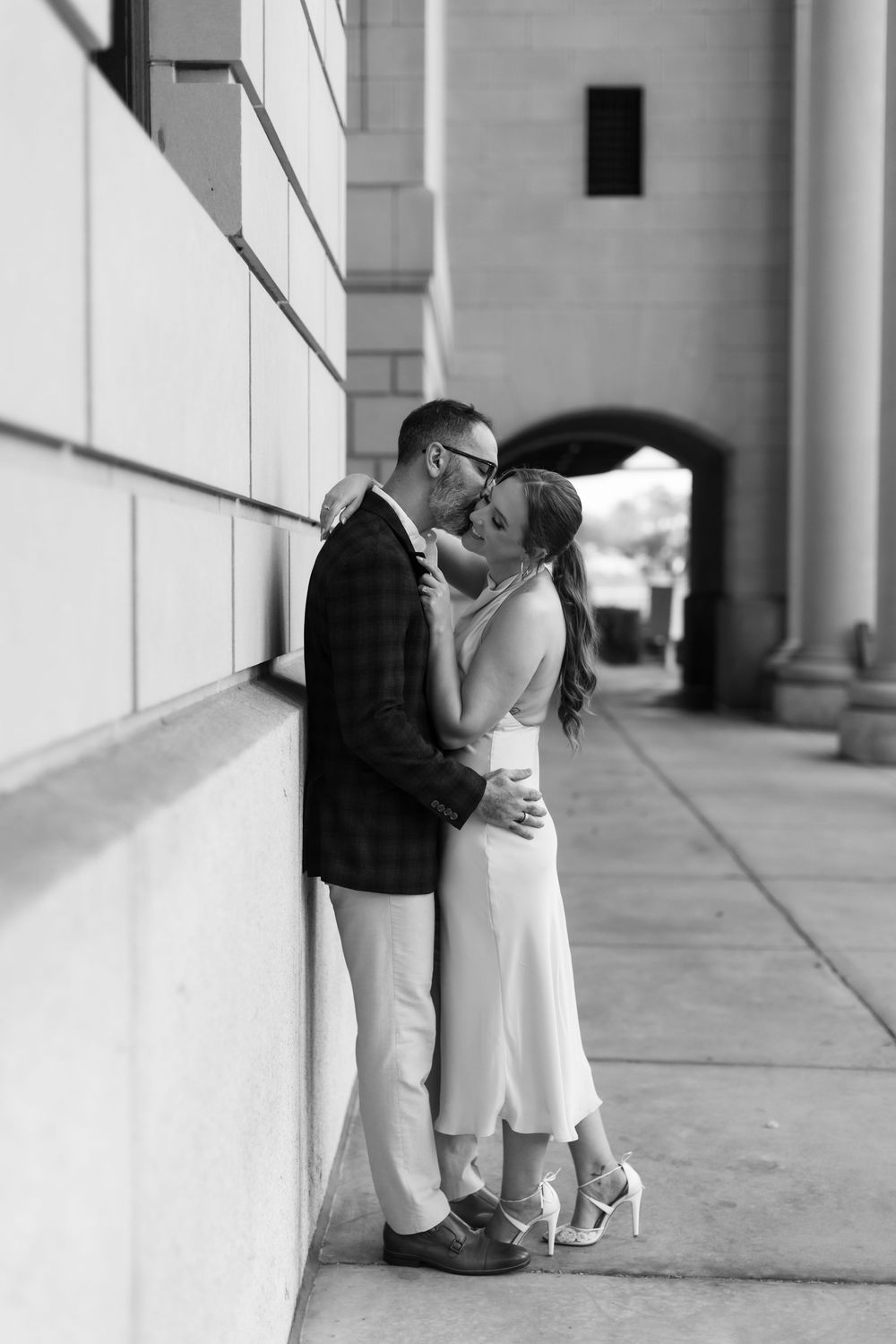 A romantic black and white photo series showing a couple embracing and kissing against a building's columns.