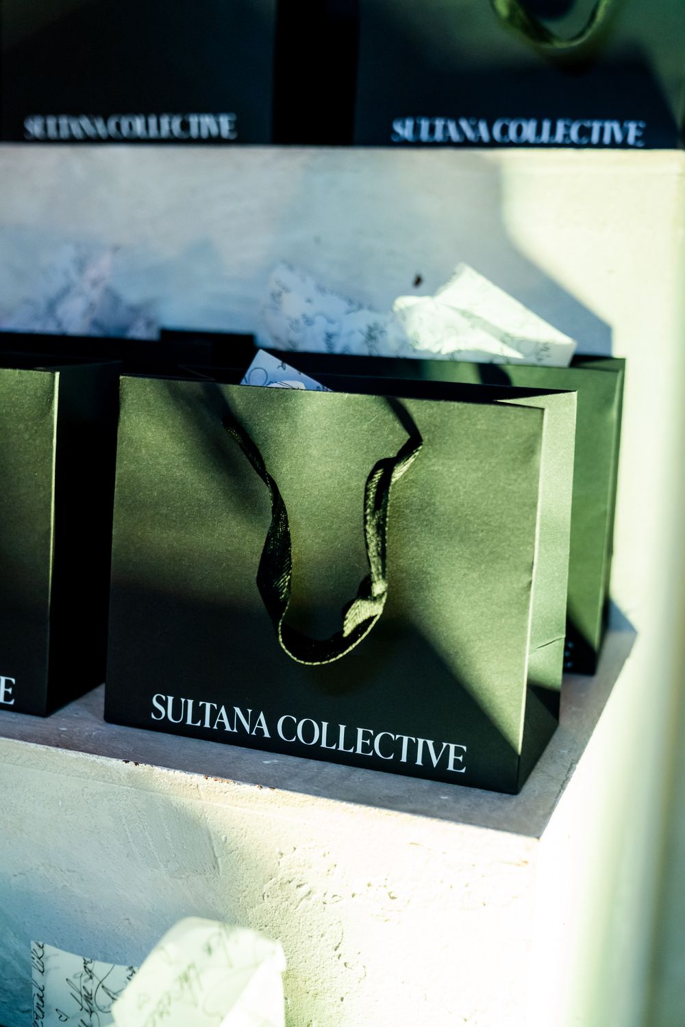 Green branded shopping bags labeled 'Sultana Collective' arranged in a retail display.