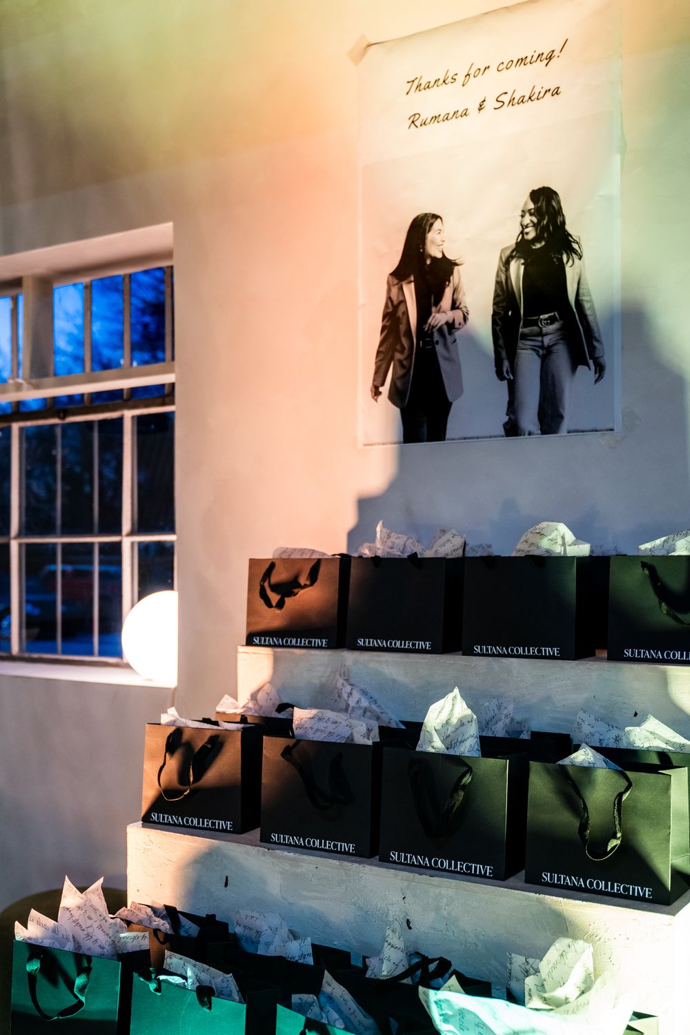 Retail display with black shopping bags arranged on shelves beneath artwork on a pink-lit wall.