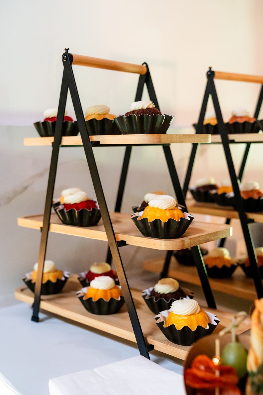 Tiered wooden display stand with mini bundt cakes arranged on multiple levels.