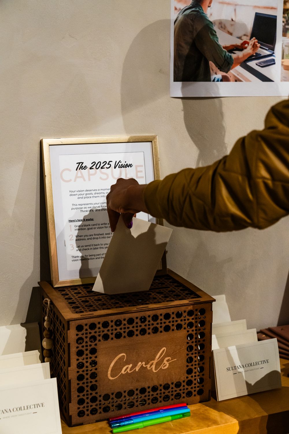 Wooden card box with illuminated text and '2025 Vision' framed document above.