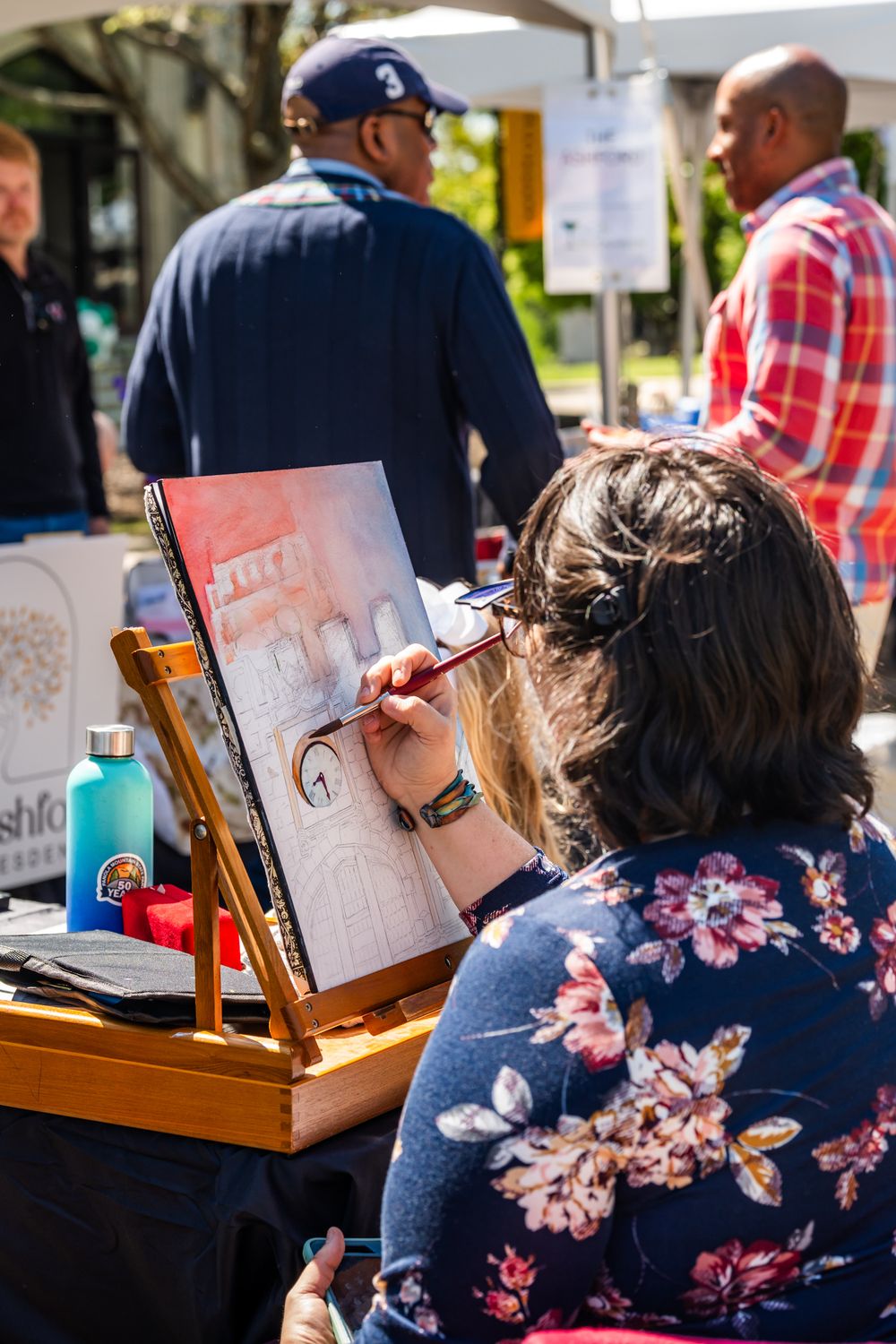 An artist working on a sketch at an outdoor event with an easel.