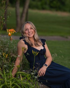 A person in a navy blue dress poses elegantly among yellow flowers in a garden setting.