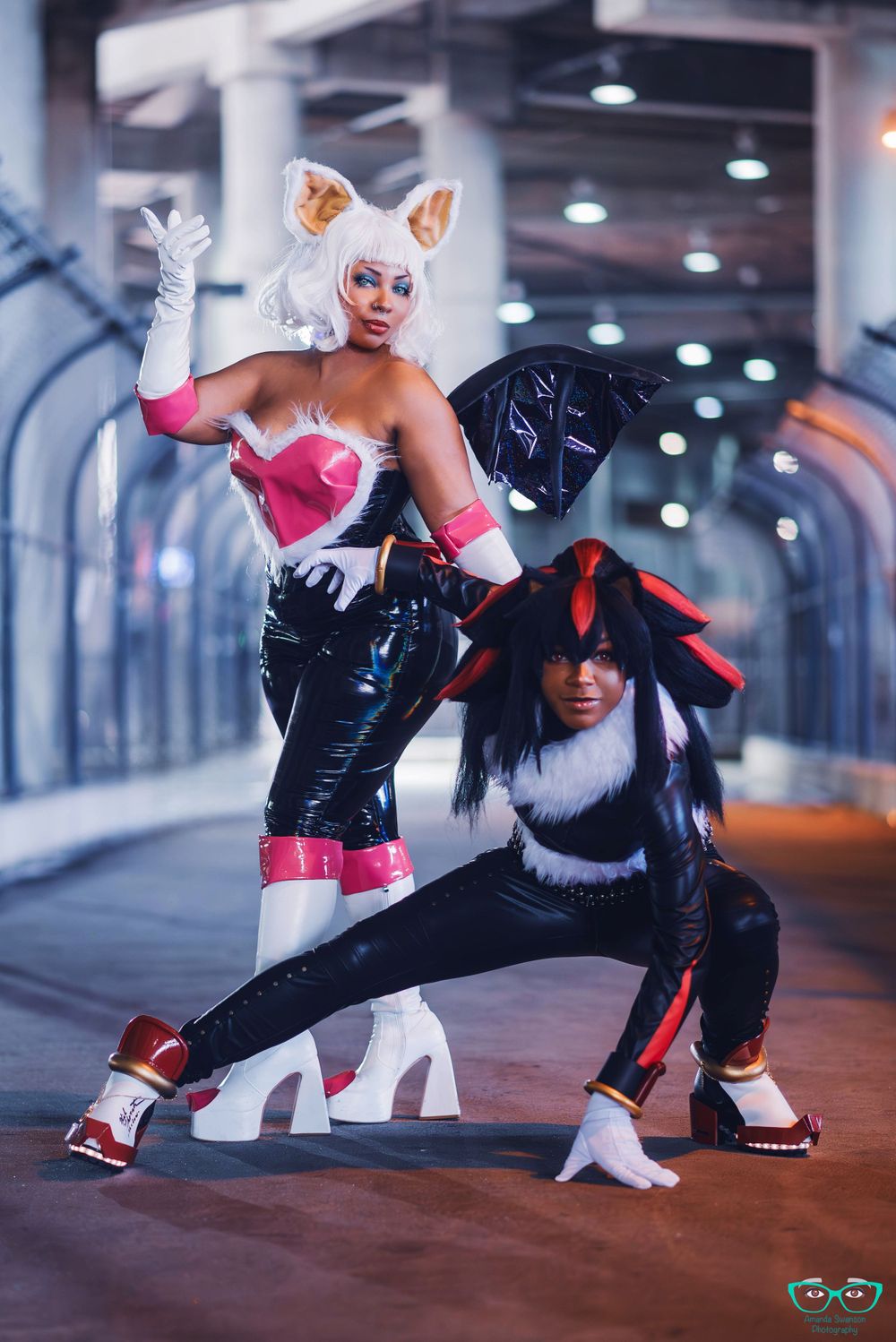 Two cosplayers pose in anime-inspired outfits featuring cat ears and dark clothing.