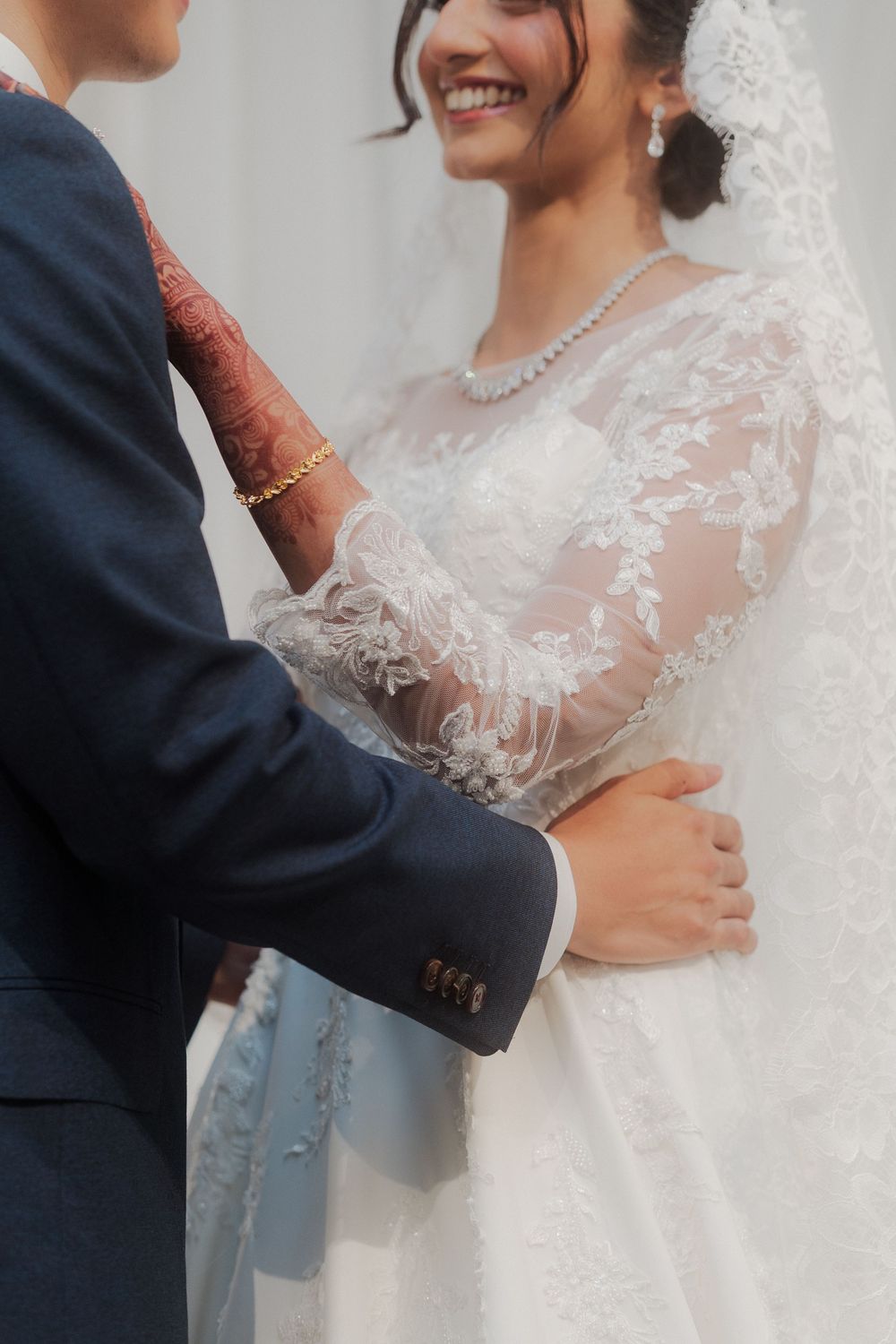 Close-up details of lace wedding dress and formal navy suit during couple portraits.