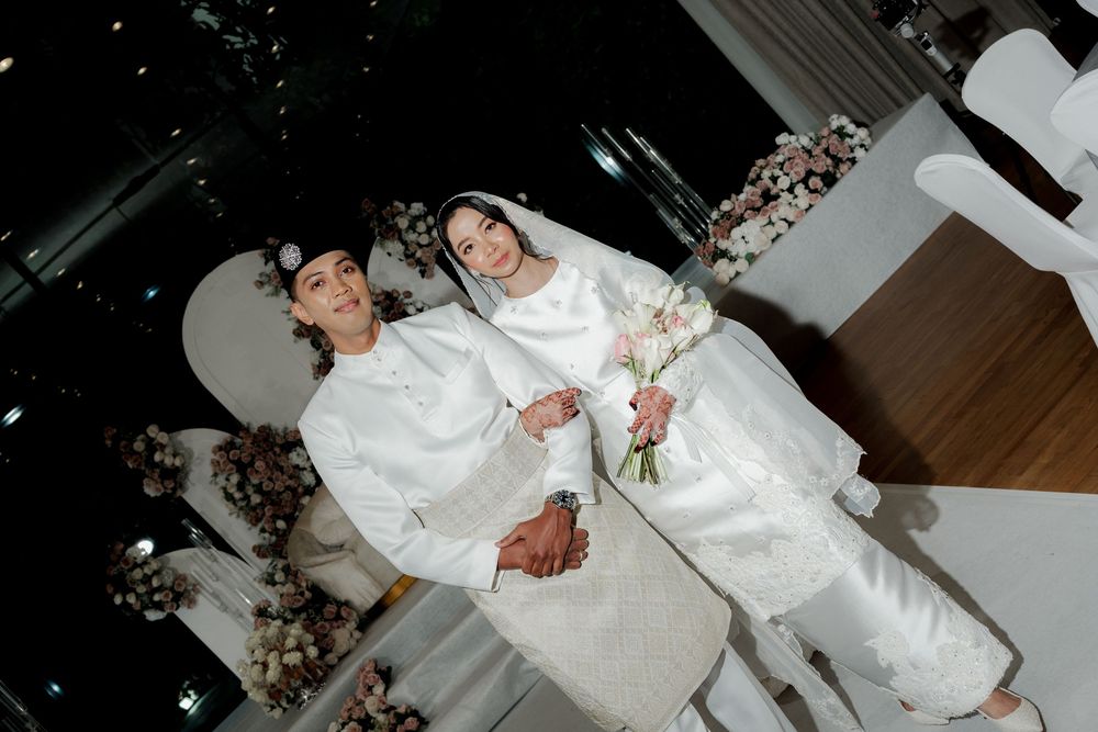 Couple in traditional white Islamic wedding attire posing together at an elegant wedding ceremony venue.