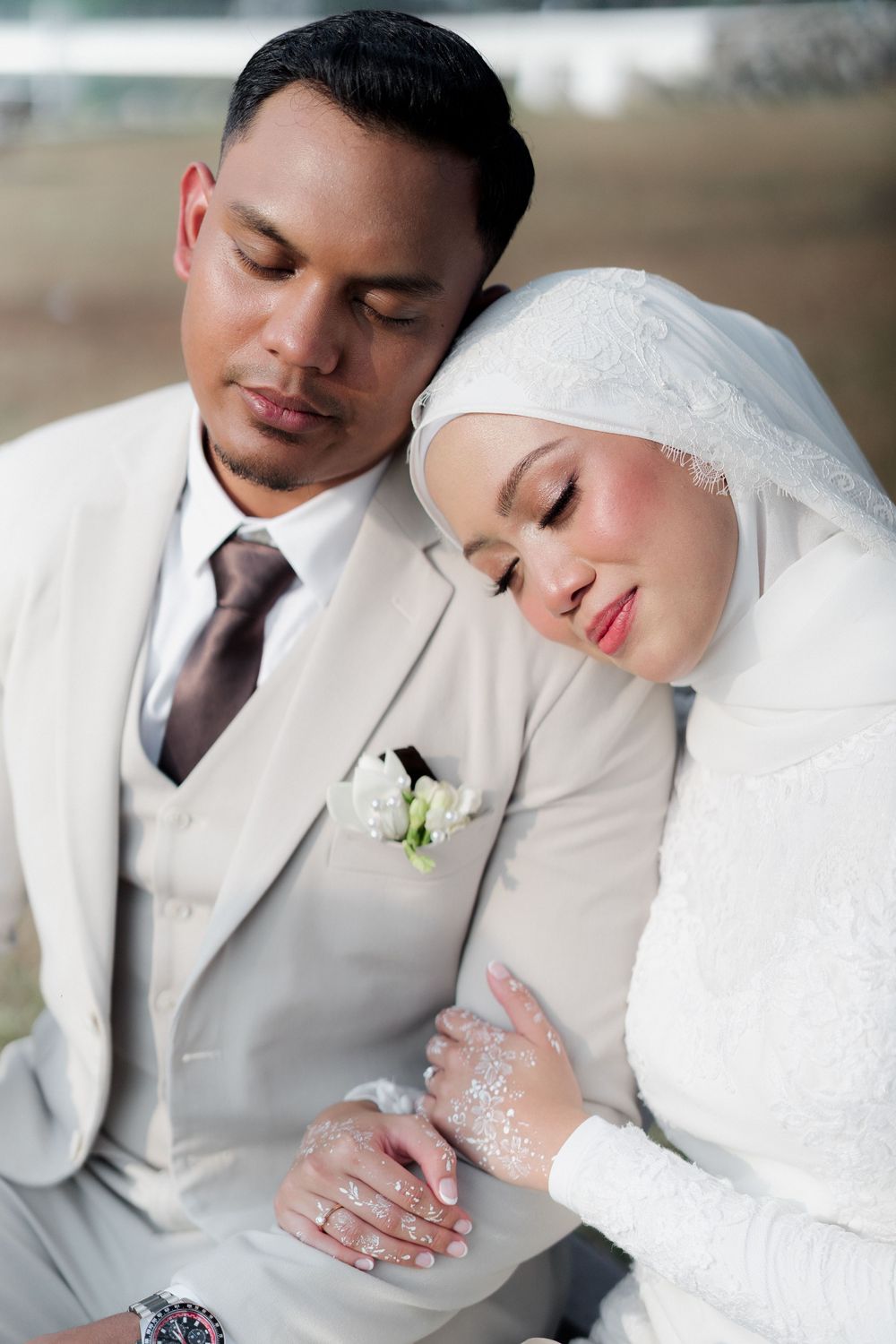 Close-up of Muslim bride in white hijab leaning on groom in beige suit during wedding photoshoot.