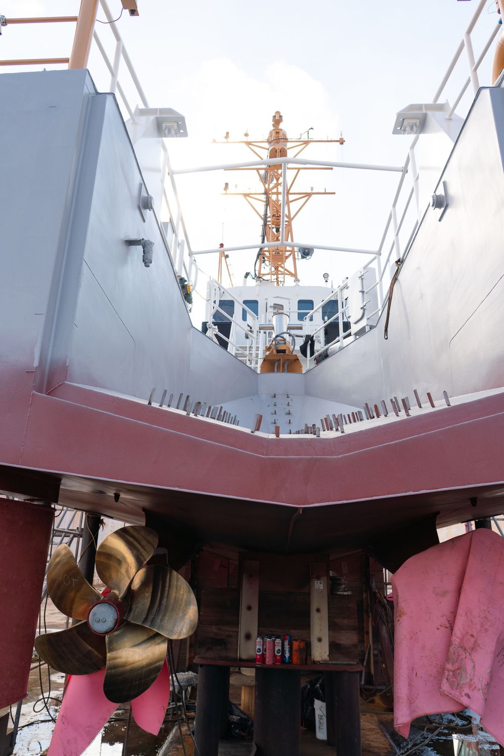 Low angle view of a ship's deck showing pink painted surfaces and maritime equipment against a cloudy sky.