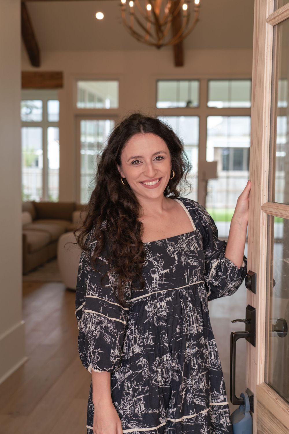 A person in a patterned dress posing in a bright room with wooden ceiling beams.