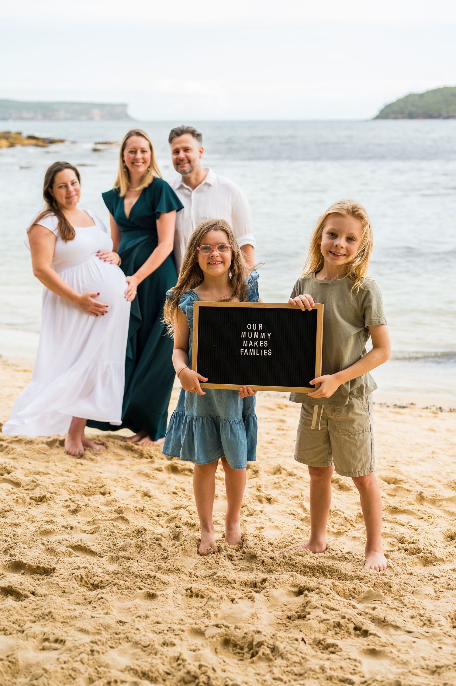 A family poses together on a sunny beach with cliffs and ocean in the background.