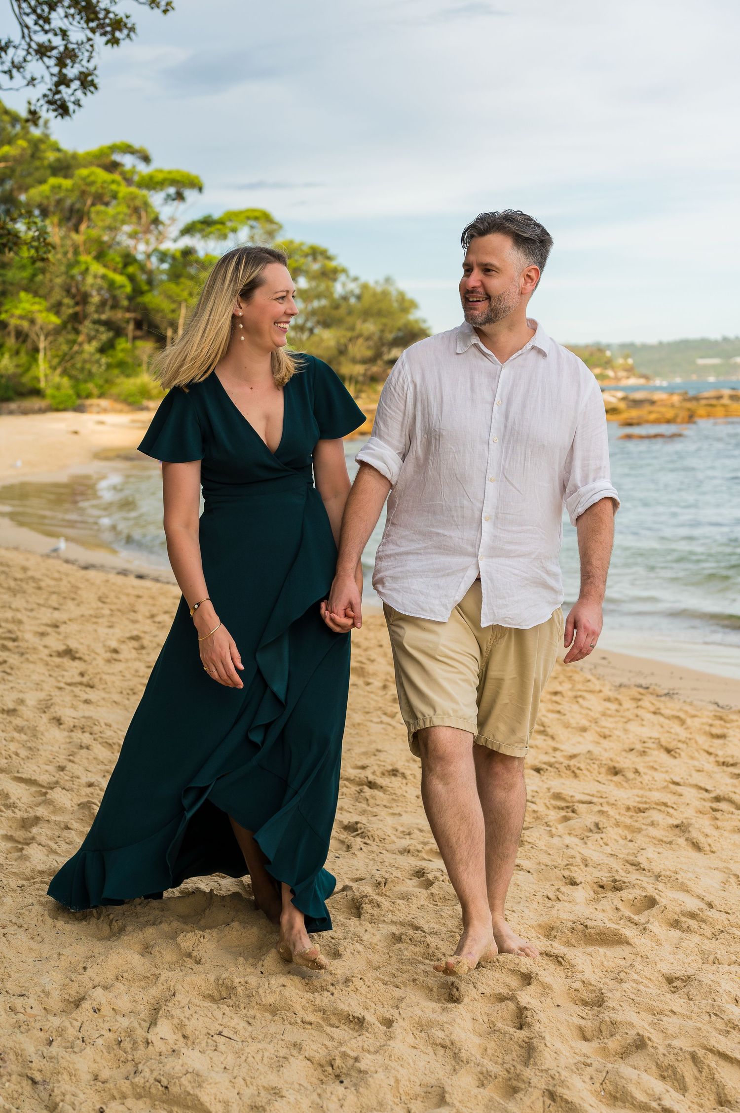 A couple shares a romantic moment sitting together on a sandy beach with ocean views in the background.