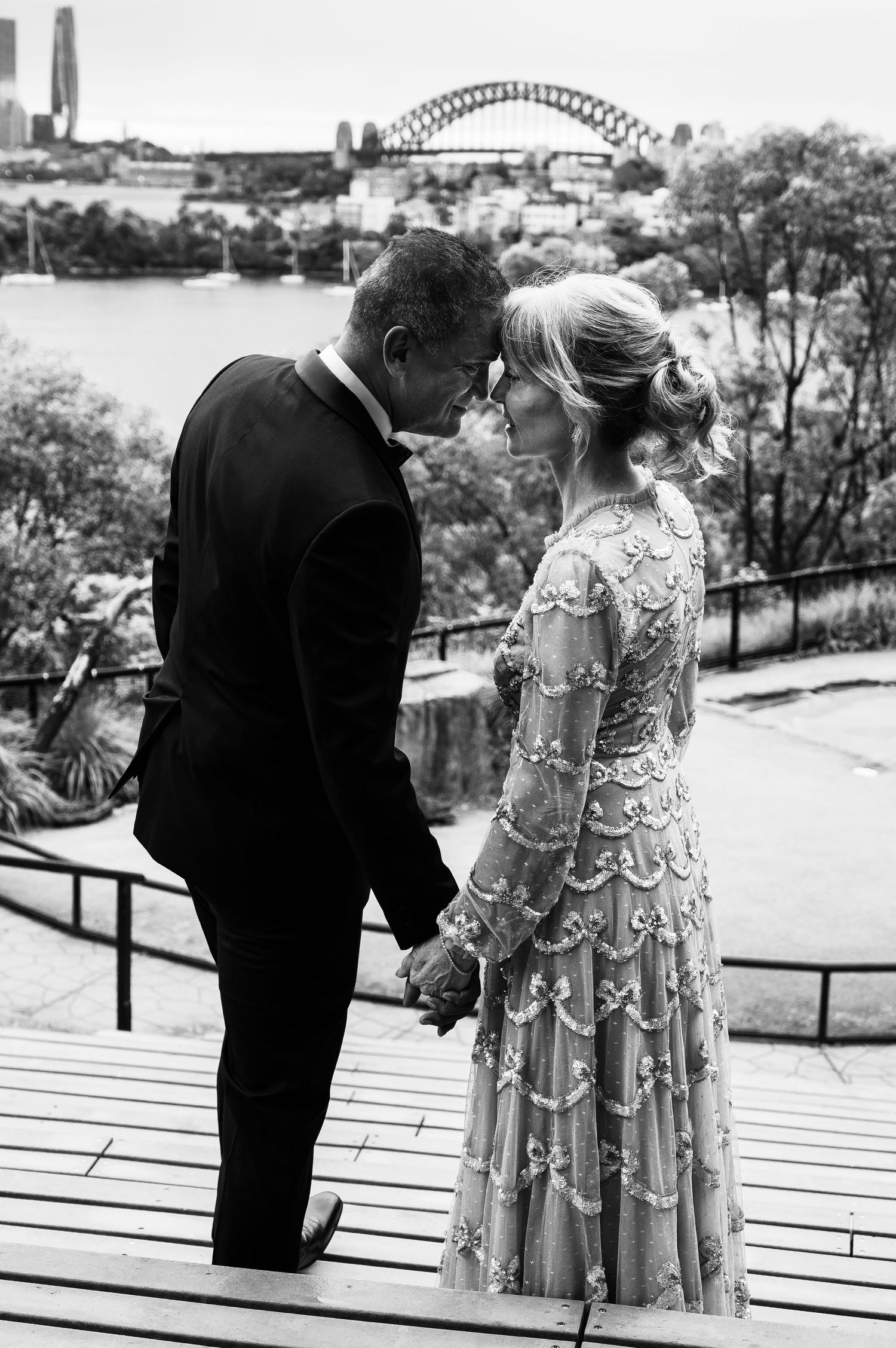 A romantic black and white photo of a couple on a deck overlooking Sydney Harbour Bridge in an intimate moment.