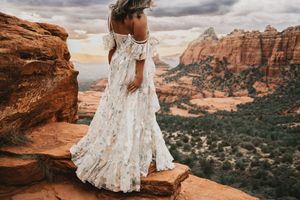 Woman in floral boho maxi dress standing on red rock overlook with stunning Zion National Park canyon views.