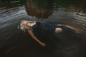 Woman in dark dress floating peacefully in calm water surrounded by reflections of trees.