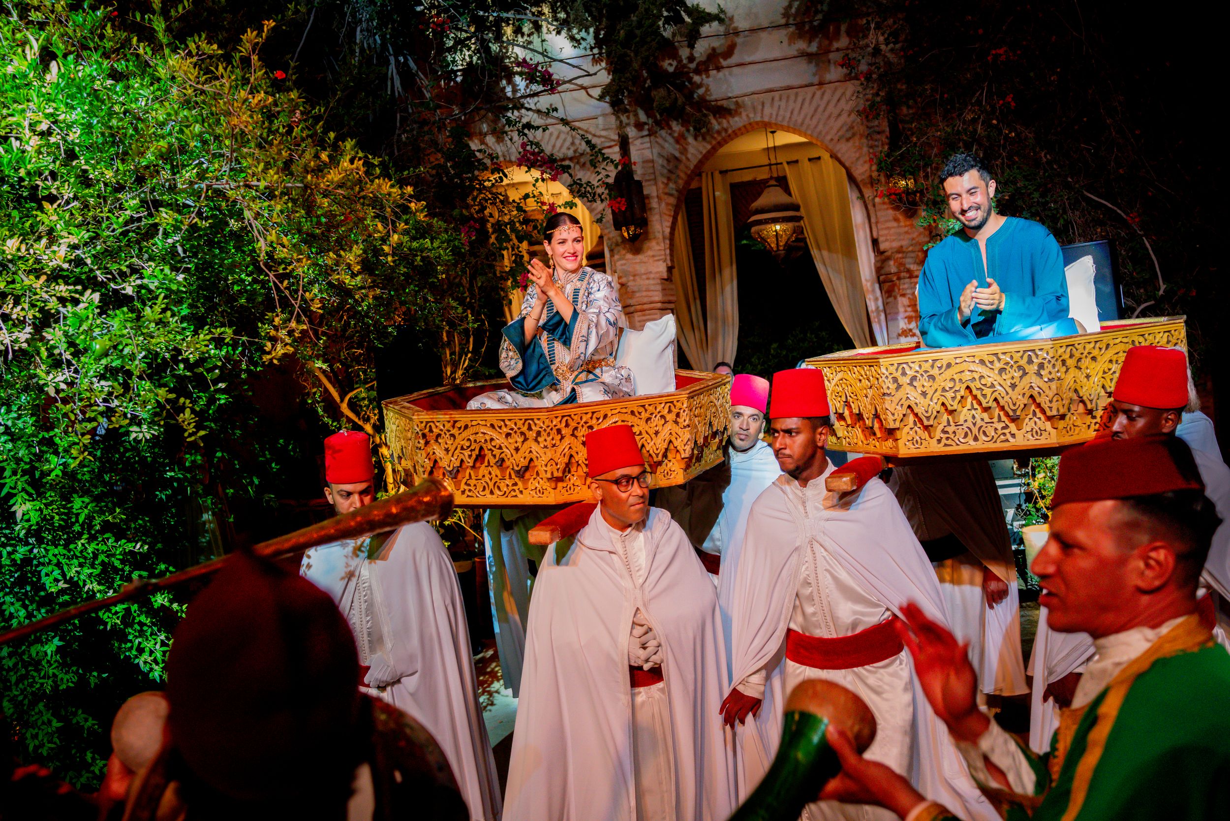 Traditional religious procession with robed clergy carrying ornate golden canopy, with celebrants in colorful attire at night.