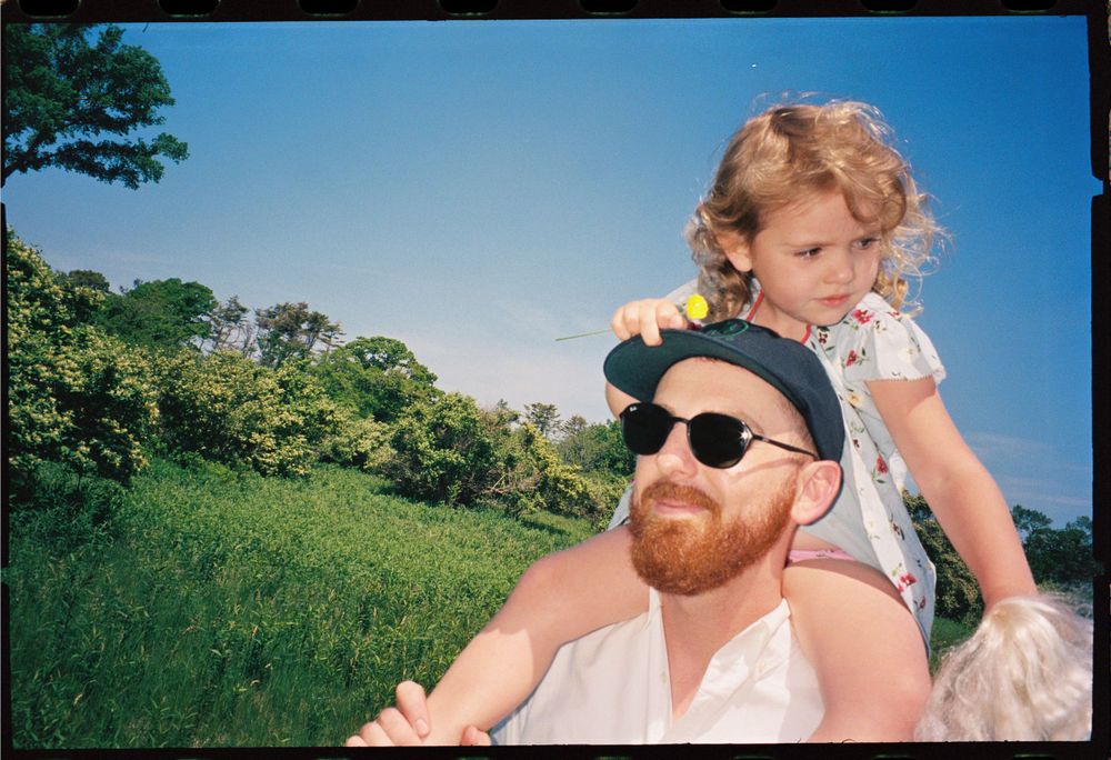A sunny outdoor portrait of an adult with sunglasses and a child enjoying nature together.