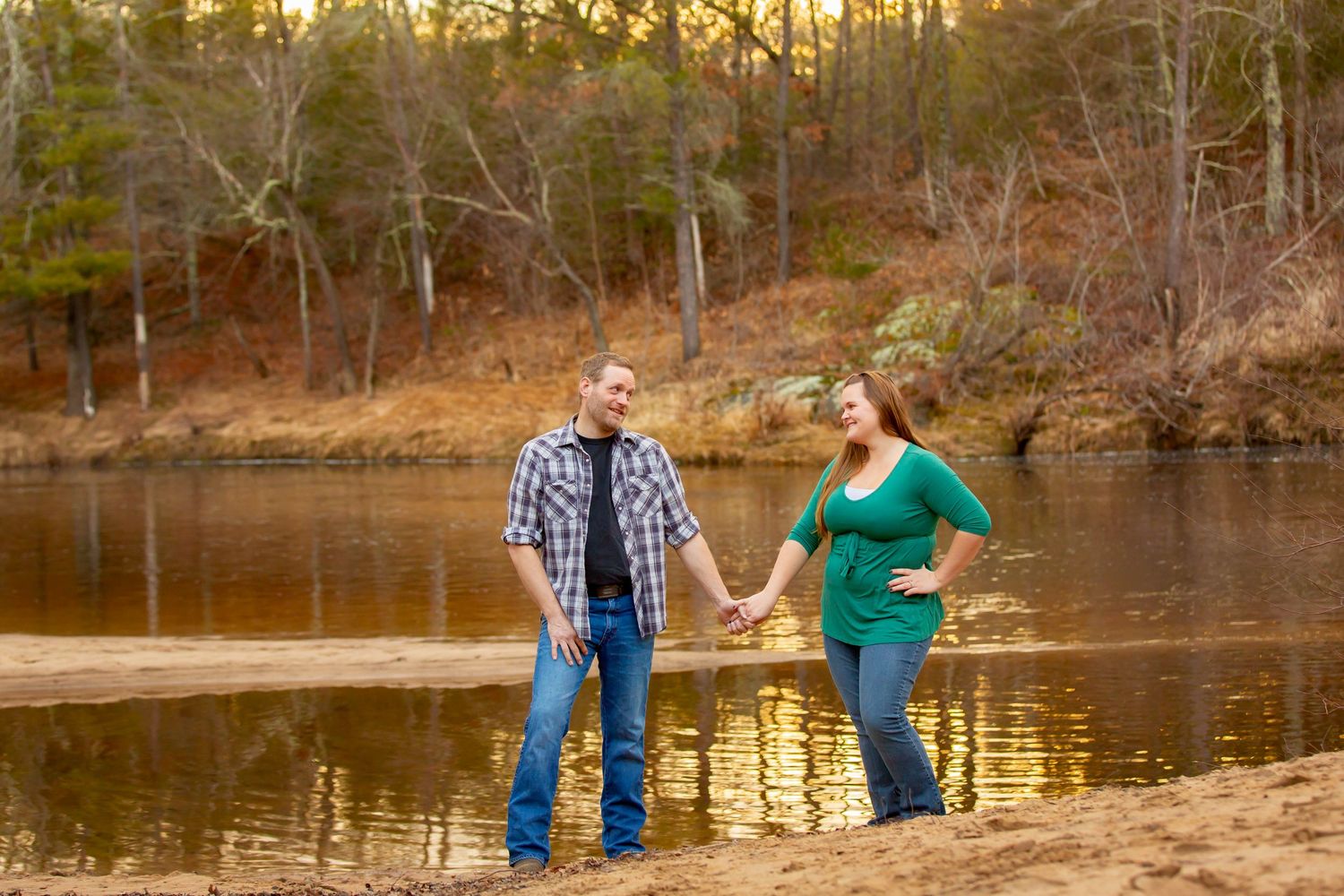 Couple holding hands by a quiet Iowa riverbank, capturing their connection amidst nature.