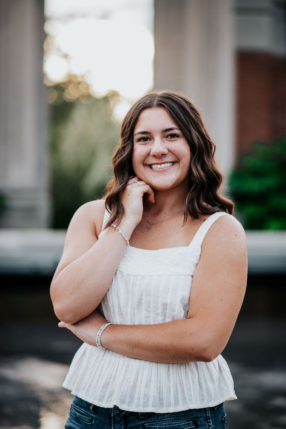 High school senior in white top and jeans posing against an architectural backdrop during senior photoshoot.