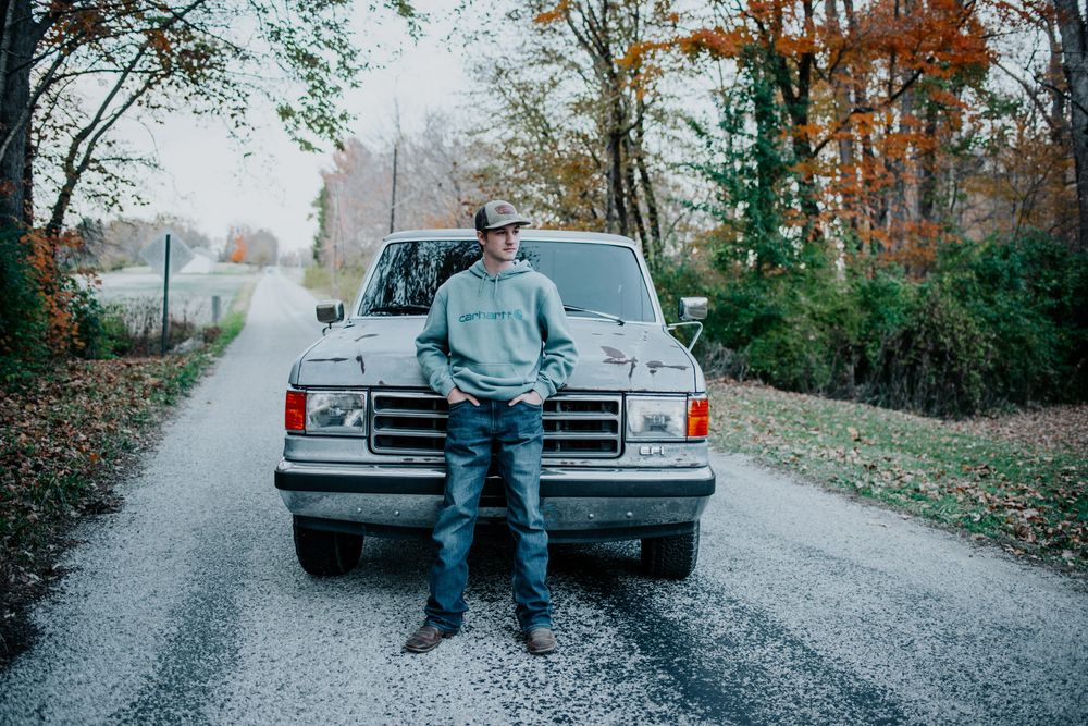 High school senior standing in front of a classic Ford pickup truck on a misty autumn road.