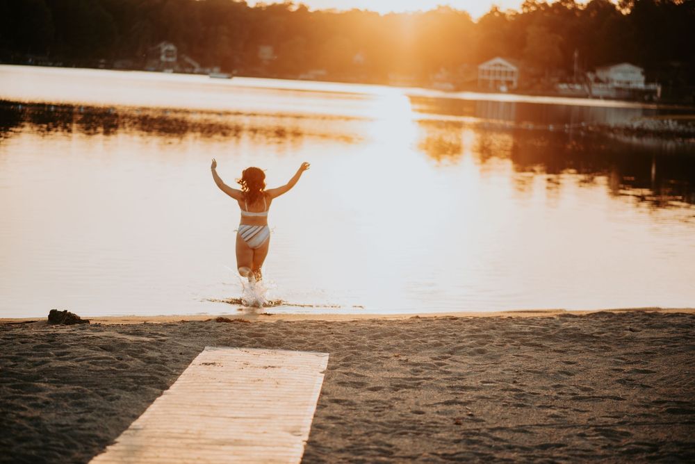 Silhouette of someone jumping joyfully on a dock during golden hour sunset over a lake during senior photoshoot.