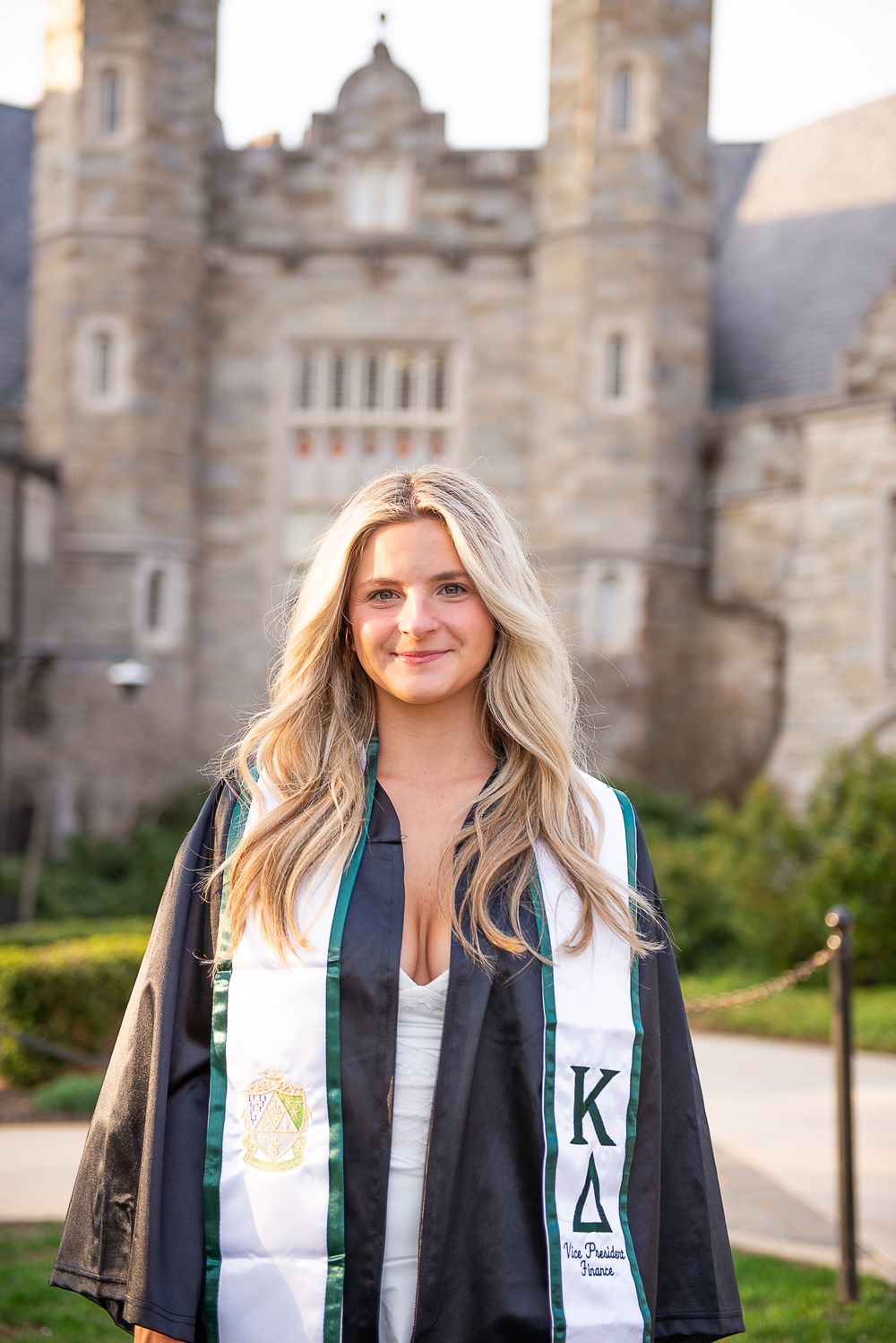 Graduate in academic regalia poses in front of West Chester University building with towers.