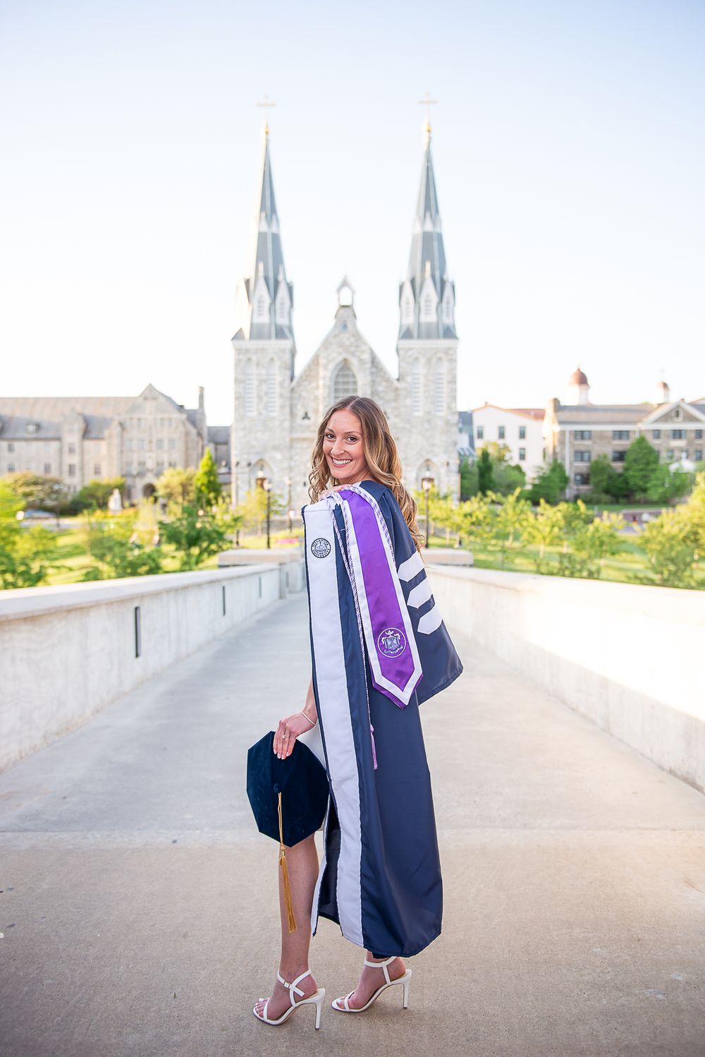 Graduate in academic regalia poses in front of St Thomas Church at Villanova.