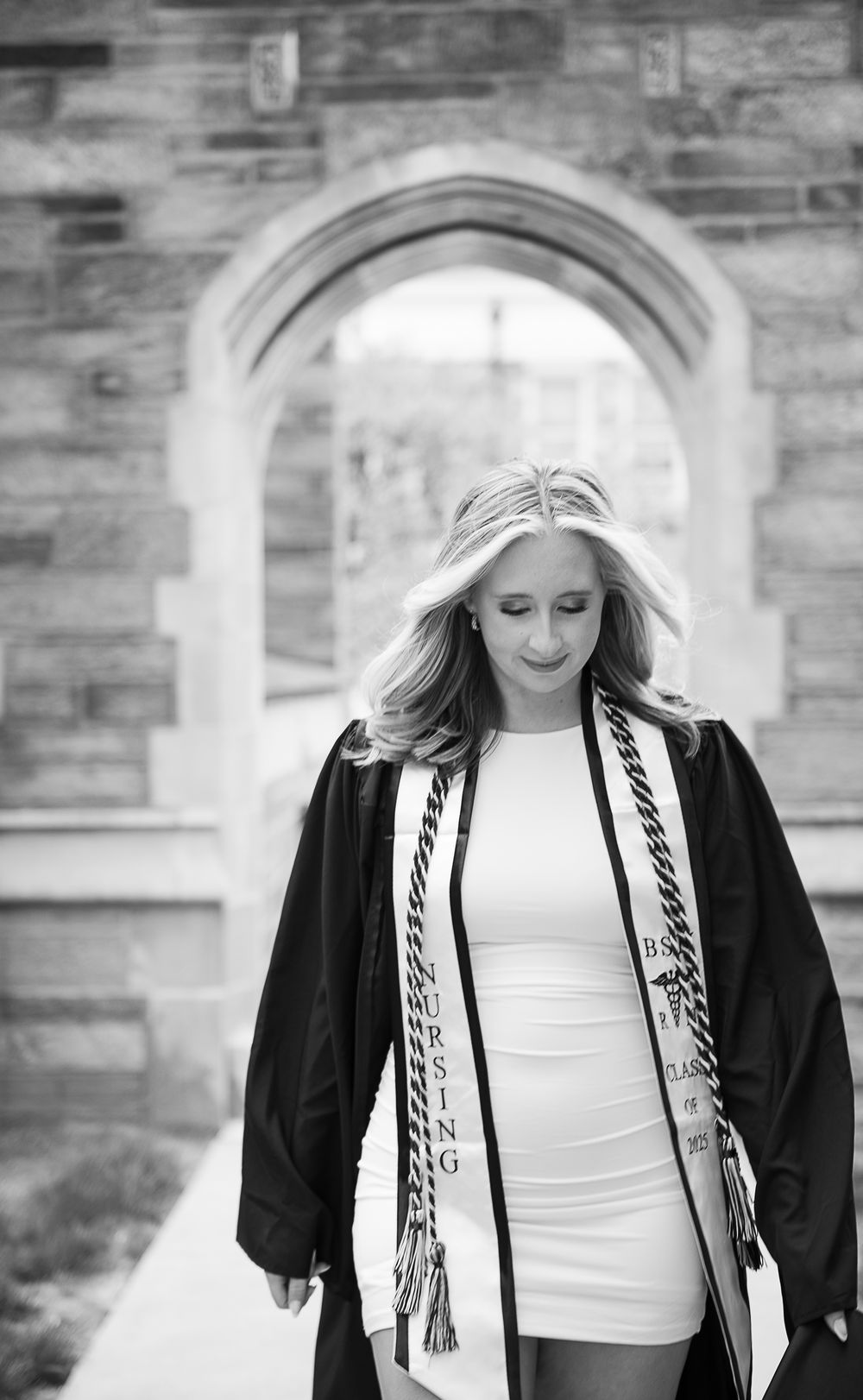 Black and white graduation portrait under stone archway showing academic regalia.