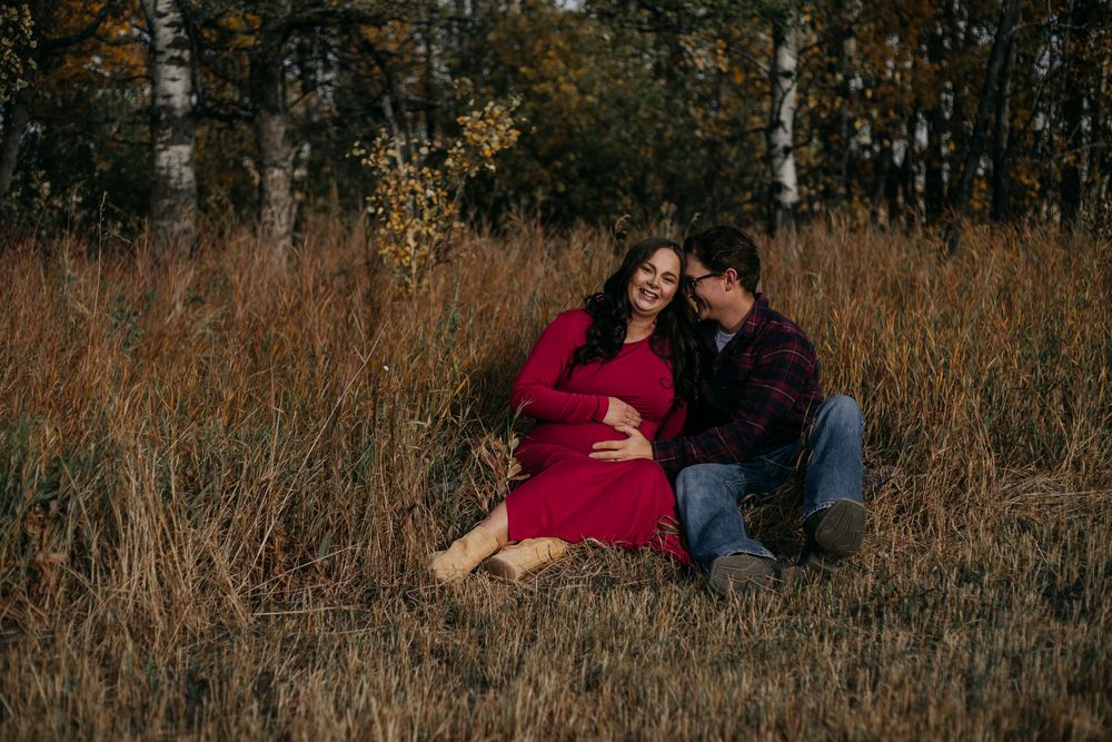 A couple sits together in a golden autumn field during sunset creating a romantic outdoor scene.