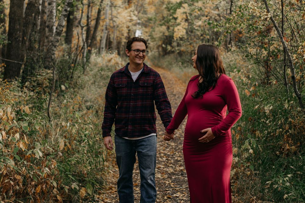 A couple walks hand in hand down a wooded autumn path surrounded by colorful fall foliage.