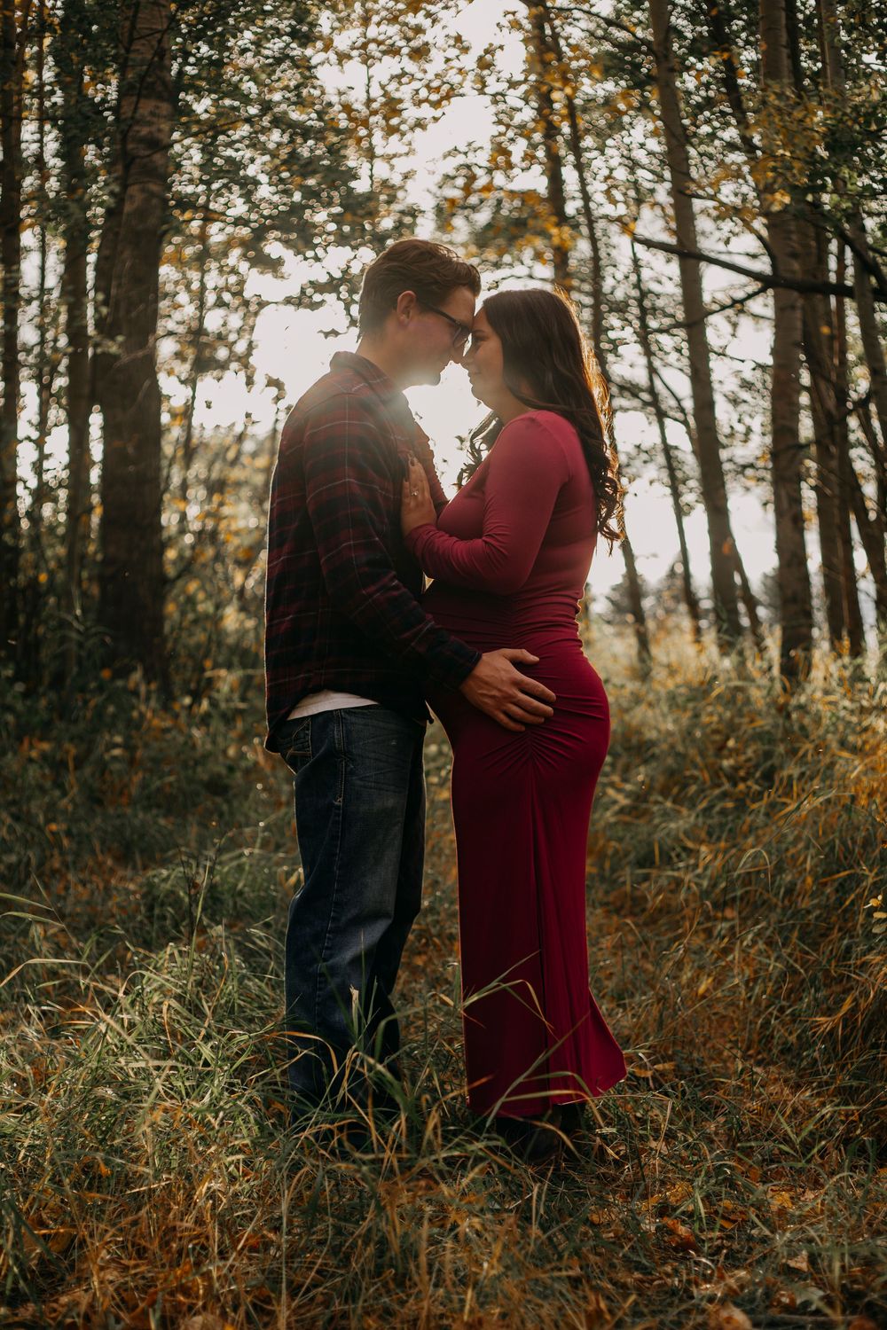 A romantic couple embraces in a sunlit forest with golden autumn foliage creating a dreamy atmosphere.