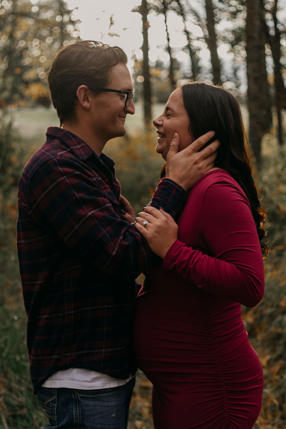 A couple shares an intimate moment in a forest setting during autumn, wearing red and plaid clothing.